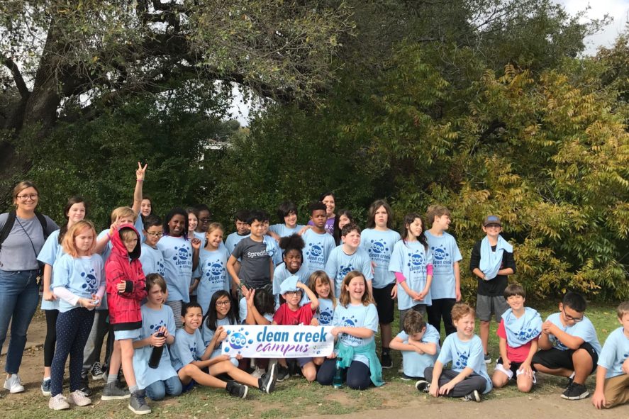 Group of students from Keep Austin Beautiful environmental education program Clean Creek Campus students wearing blue t-shirts in front of tall trees