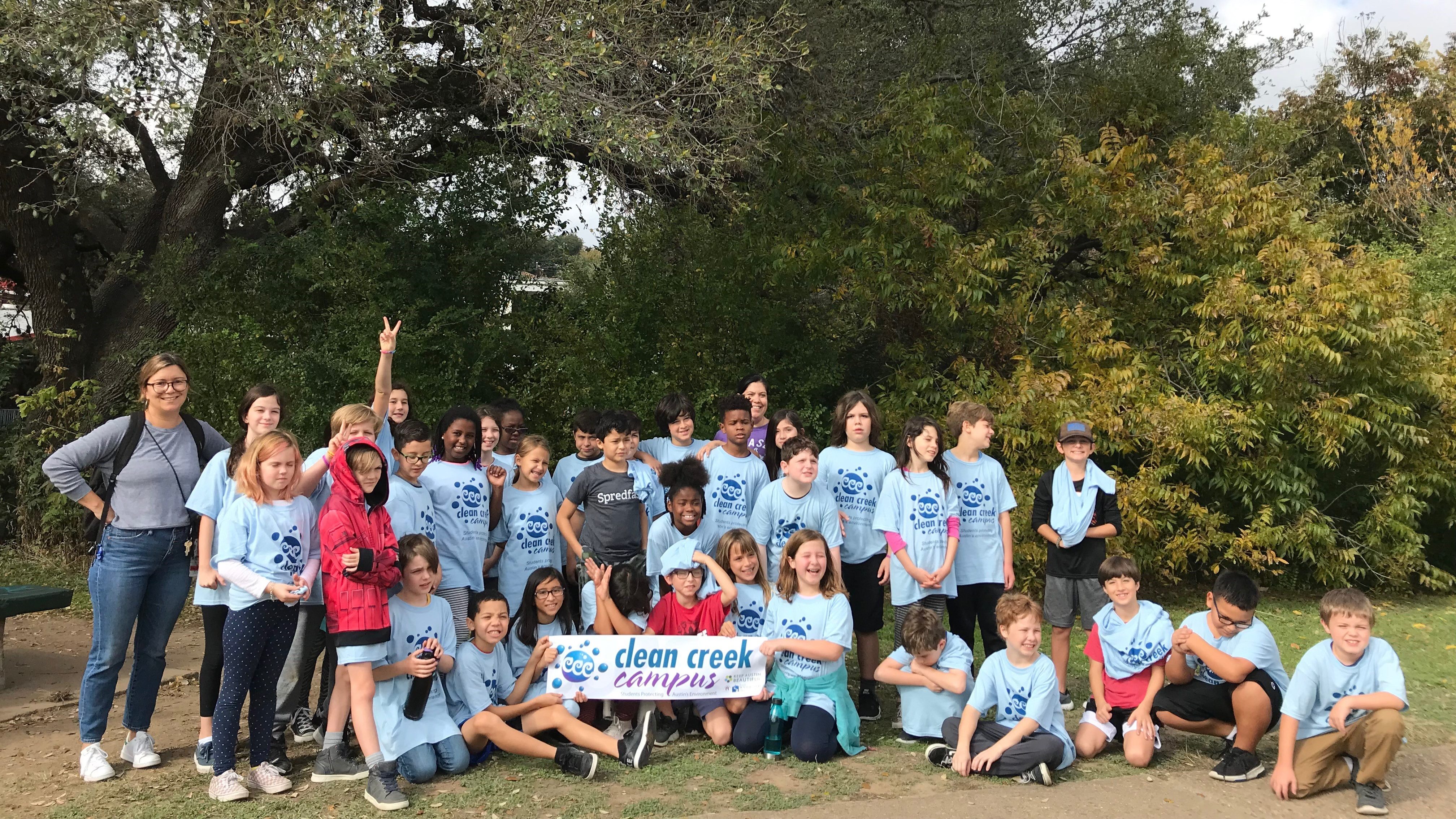 Group of students from Keep Austin Beautiful environmental education program Clean Creek Campus students wearing blue t-shirts in front of tall trees