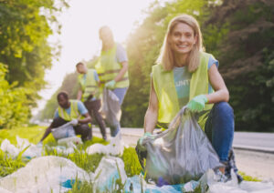 Several volunteers in reflective vests pick up trash on the side of the road.