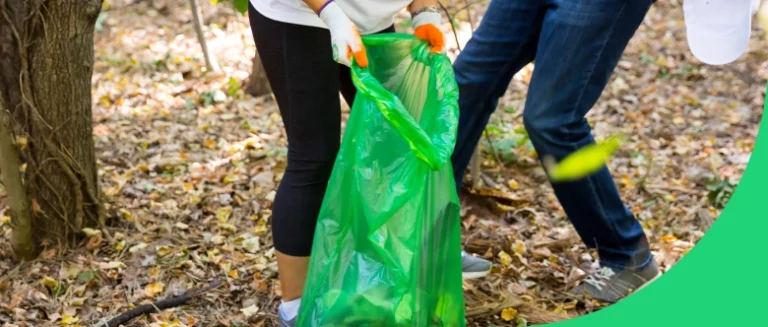 A volunteer with a green trash bag in a park.