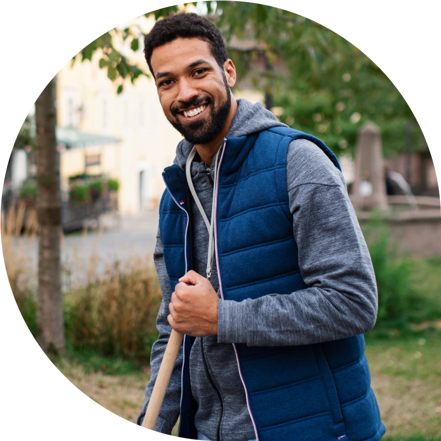 Man in a gray hoodie and navy vest smiles at the camera.