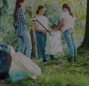 Four women gathered around a trash bag, putting trash inside.