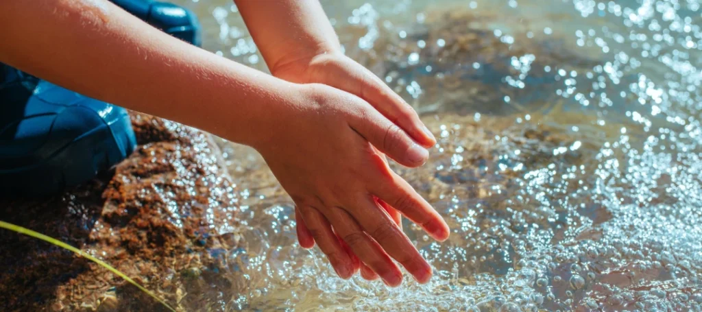 Close-up of a person washing their hands in a creek.