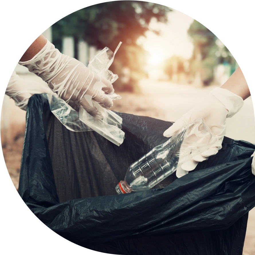 Two gloves hands placing trash into a black trash bag.