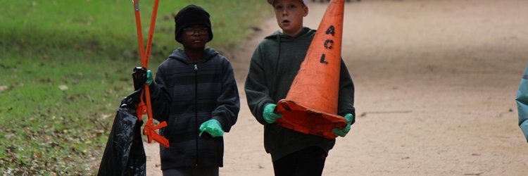 Two young boys walking down a gravel path. One carries an orange traffic cone.