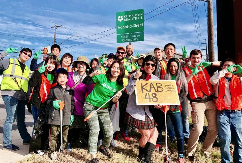 A group of people gathered around a Keep Austin Beautiful Adopt-a-Street sign.