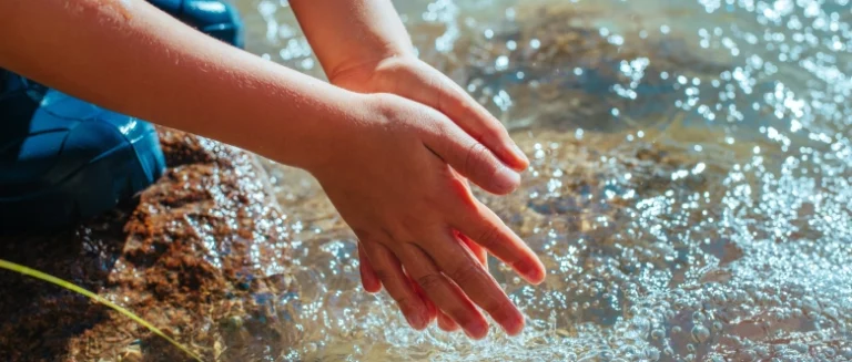 Close-up of a young child washing their hands in an Austin creek.