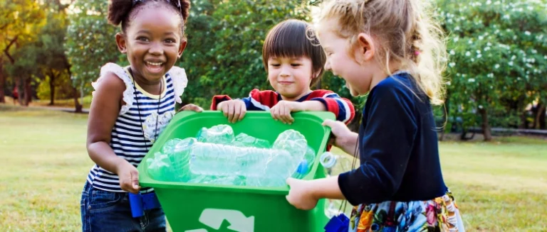 Three children gathered around a recycling bin.